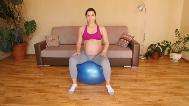 Νεαρή έγκυος γυναίκα που κάνει ασκήσεις γυμναστικής σε μπάλα γυμναστικής. Ασκήσεις για έγκυες γυναίκες. Γυμναστική στο σπίτι. — Αρχείο Βίντεο