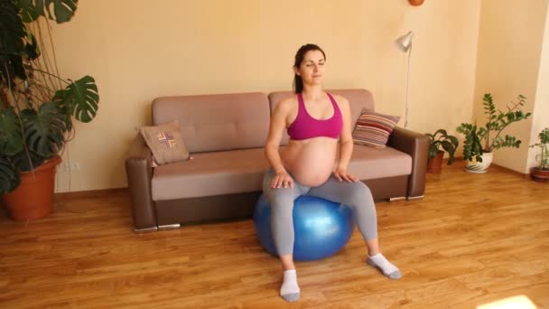 Jeune femme enceinte faisant des exercices de fitness sur une balle de fitness. Exercices pour les femmes enceintes. Fitness à la maison. Glissez. Mouvement de caméra. — Video