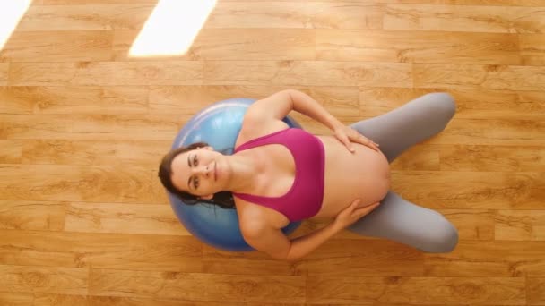 Mujer embarazada joven haciendo ejercicios de fitness en una pelota de fitness. Ejercicios para mujeres embarazadas. Fitness en casa. Levanta la pelvis. Movimiento de cámara. Vista superior . — Vídeos de Stock