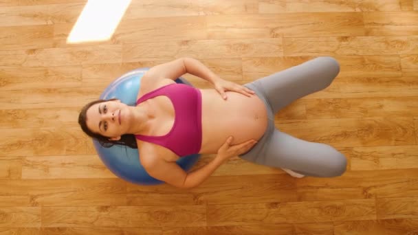 Mujer embarazada joven haciendo ejercicios de fitness en una pelota de fitness. Ejercicios para mujeres embarazadas. Fitness en casa. Levanta la pelvis. Vista superior . — Vídeos de Stock