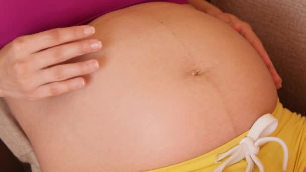 Fehér krém csöpög a terhes nők hasára. Egy fiatal terhes nő krémet tesz a gyomrára. Egy terhes nő megsimogatja a hasát. Közelkép — Stock videók
