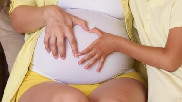 Женская рука и рука ребенка делают сердце на животе беременной женщины. Семейные ценности. В ожидании рождения. Живот беременной женщины. Крупный план — стоковое видео