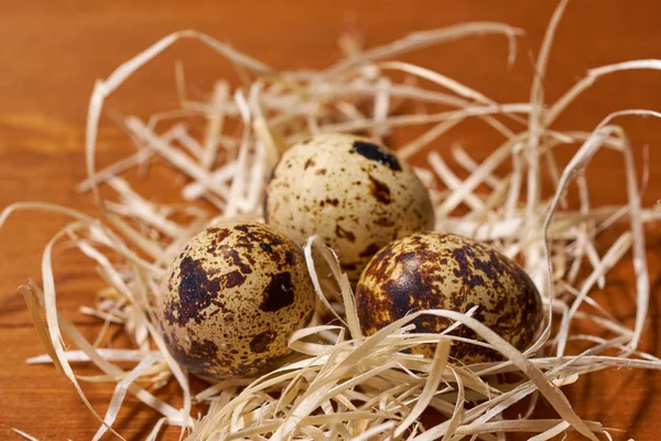 Quail eggs  in straw nest on brown wooden background. Selective focus — Stock Photo, Image