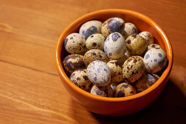 Quail eggs in clay bowl on brown wooden background. Selective focus — Stock Photo, Image