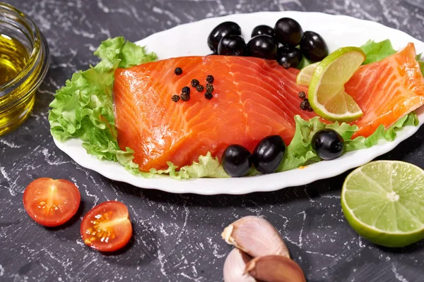 Un trozo de salmón en un plato blanco con aceitunas y limón, sobre un fondo gris. Enfoque selectivo —  Fotos de Stock