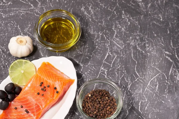 Een stuk zalm op een witte plaat met olijven en citroen, op een grijze achtergrond. Selectieve aandacht. ruimte voor tekst. — Stockfoto