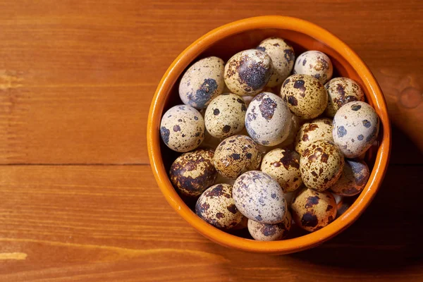 Quail eggs in clay bowl on brown wooden background. Selective focus — Stock Photo, Image