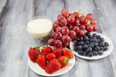 Çilek, yabanmersini yoğurt ve gri bir ahşap zemin üzerinde üzüm ile