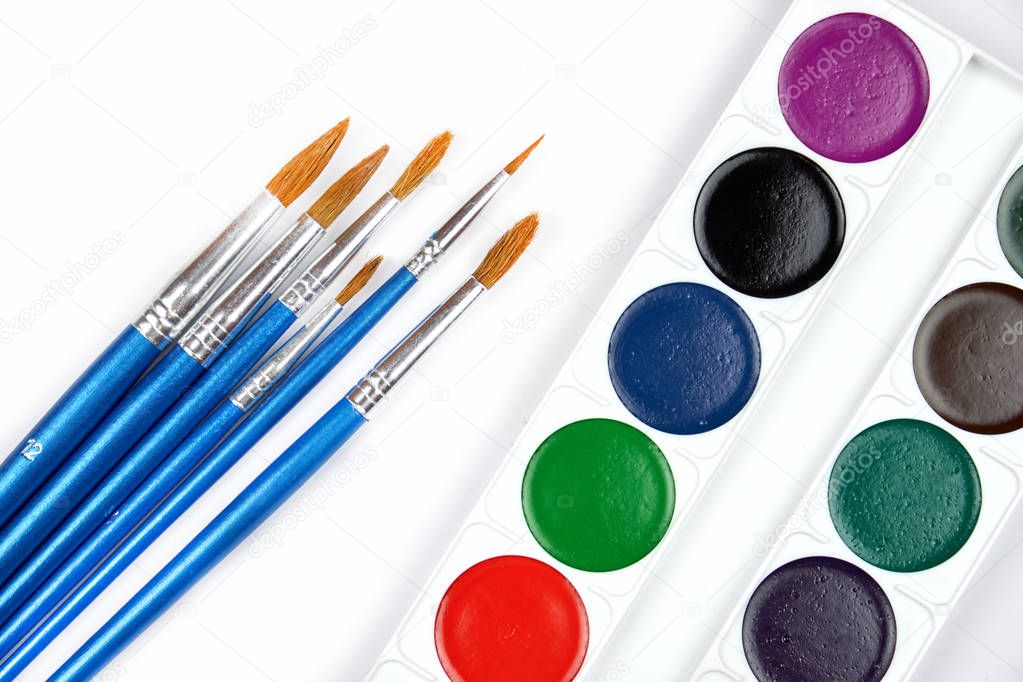 A palette of watercolor paints and brushes of different sizes, lying on a gray wooden background