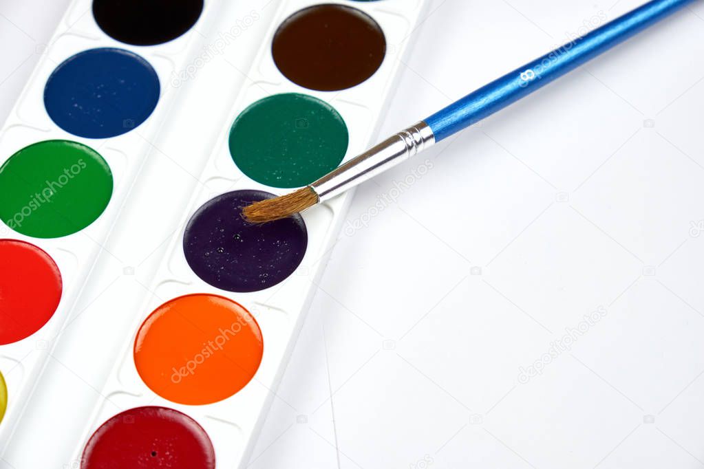 A palette of watercolor paints and brushes of different sizes, lying on a gray wooden background
