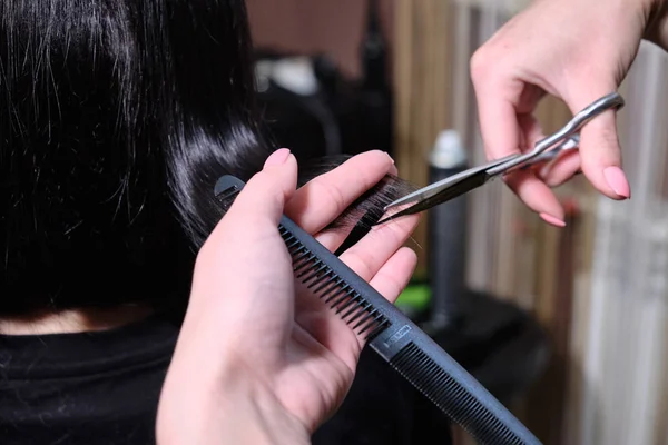美发师使一个发型的黑发女孩在美容院与剪刀和梳子 . — 图库照片