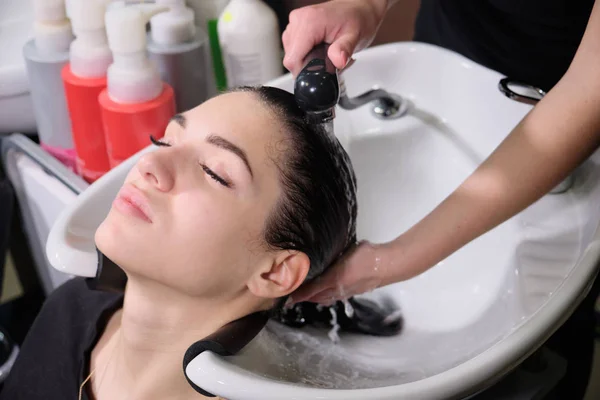 Cabeleireiro lava o cabelo com xampu para menina morena em um salão de beleza — Fotografia de Stock