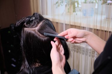 Kuaför Curling demir ile bir güzellik salonunda bir saç modeli esmer kız yapar.