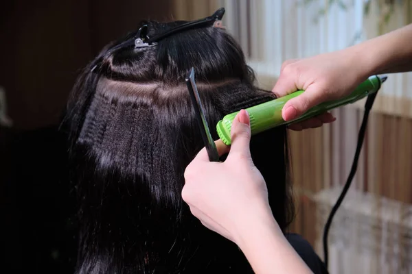 Cabeleireiro faz uma menina morena penteado em um salão de beleza com ferro Curling . — Fotografia de Stock