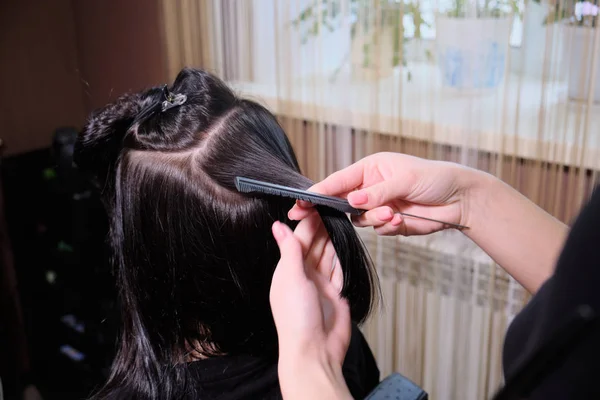Cabeleireiro faz uma menina morena penteado em um salão de beleza com ferro Curling . — Fotografia de Stock