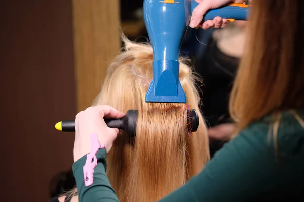 Fryzjer sprawia, że fryzura blond dziewczyna w salonie piękności z suszarką do włosów — Zdjęcie stockowe