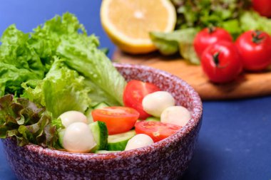 Taze sebzeler ve mavi bir arka planda mozzarella ile bir kase salata. Caprese salatası. Marul, kiraz domates, mozzarella, 