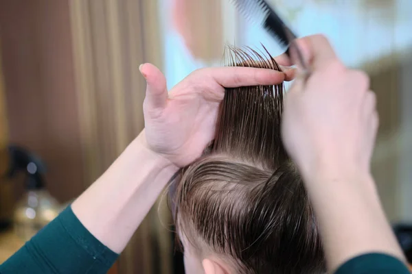 Barbeiro. Cabeleireiro faz penteado para um menino com tesoura de cabelo e pente preto . — Fotografia de Stock