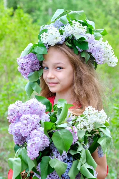 A girl with a bouquet of lilacs and a wreath of lilacs on her head in spring garden