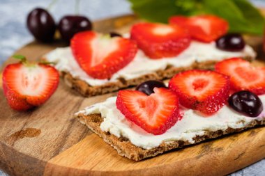 süzme peynir, taze çilek ve kiraz ahşap bir tahta üzerinde, gri bir arka planda, seçici odak ile ekmek