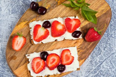 süzme peynir, taze çilek ve kiraz ahşap bir tahta üzerinde, gri bir arka planda, seçici odak ile ekmek