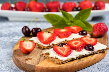 peynir, çilek ve kiraz ile somun bir kesme tahtası ve nane yaprakları ile gri arka plan