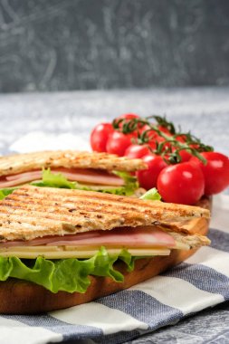 Ahşap tahta üzerinde bir üçgen şeklinde bir sandviç yarısı. Sandviç, marul yaprağı ve kiraz domatesleriyle dekore edilmiştir..