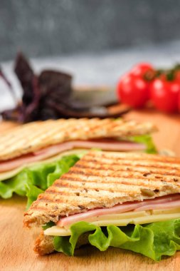 Ahşap tahta üzerinde bir üçgen şeklinde bir sandviç yarısı. Sandviç, marul yaprağı ve kiraz domatesleriyle dekore edilmiştir..