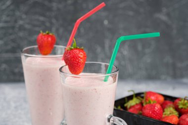 Gri arka plan üzerinde cam kenarında çilek parçaları ile çilek milkshake ile iki bardak.