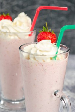 Gri arka plan üzerinde cam kenarında çilek parçaları ile çilek milkshake ile iki bardak.