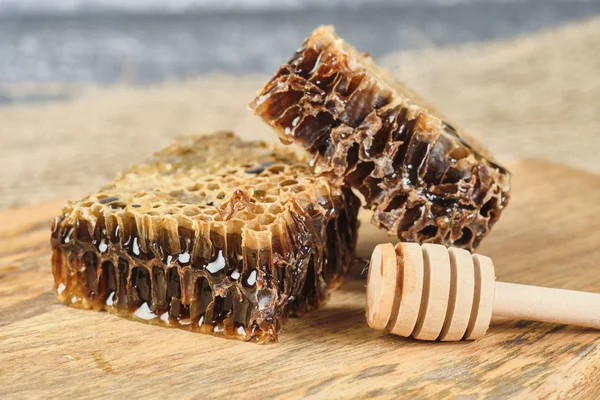 Favo de mel com mel em uma tábua de madeira, e uma colher de mel, foco seletivo — Fotografia de Stock