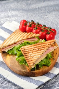 Ahşap tahta üzerinde bir üçgen şeklinde bir sandviç yarısı. Sandviç, marul yaprağı ve kiraz domatesleriyle dekore edilmiştir..