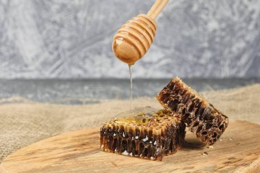 ahşap bir Tahta üzerinde bal ile petek, bal için bir kaşık ile yavaş yavaş bal seçici odak döker