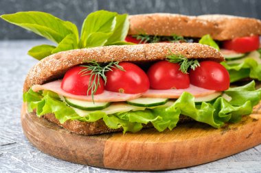 Ahşap tahta üzerinde peynir, salatalık ve kiraz domates ile sandviç. Sandviç, marul yaprağı ve kiraz domatesleriyle dekore edilmiştir..