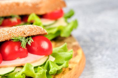Ahşap tahta üzerinde peynir, salatalık ve kiraz domates ile sandviç. Sandviç, marul yaprağı ve kiraz domatesleriyle dekore edilmiştir..