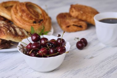 taze kiraz bir kase ve beyaz ahşap arka plan üzerinde bir fincan çay ile beyaz bir tabak üzerinde kiraz ile puffs. Close. Seçici odaklama