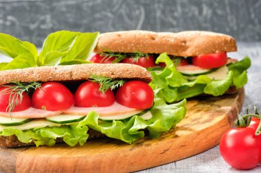 Ahşap tahta üzerinde peynir, salatalık ve kiraz domates ile sandviç. Sandviç, marul yaprağı ve kiraz domatesleriyle dekore edilmiştir..