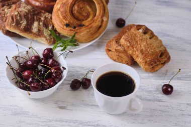 taze kiraz bir kase ve beyaz ahşap arka plan üzerinde bir fincan çay ile beyaz bir tabak üzerinde kiraz ile puffs. Close. Seçici odaklama