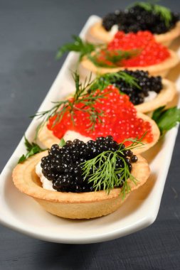 gri bir arka plan üzerinde limon ile beyaz bir tabak üzerinde kırmızı ve siyah havyar ile tartlets. Close