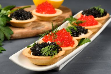 gri bir arka plan üzerinde limon ile beyaz bir tabak üzerinde kırmızı ve siyah havyar ile tartlets. Close