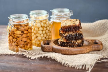 ahşap bir tabak üzerinde petek bal. Arka planda limon ve zencefil ile bal ve badem ve fındık ile Kavanoz