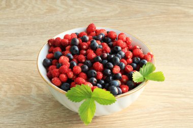 Beyaz seramik tabakta ahşap bir masada çilek ve yaban mersini.