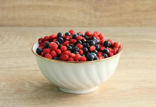 Beyaz seramik tabakta ahşap bir masada çilek ve yaban mersini.