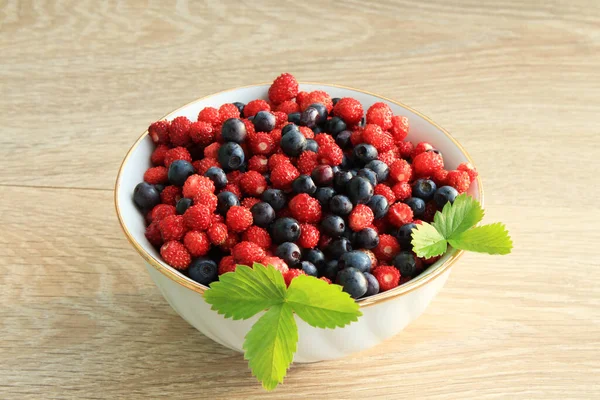 Beyaz seramik tabakta ahşap bir masada çilek ve yaban mersini.