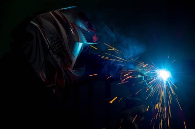 male welder in a mask performing metal welding. photo in dark colors. sparks flying. clipart