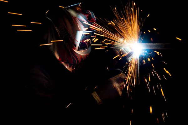 执行金属焊接的面罩中的男焊工。照片为深色。火花飞舞. — 图库照片