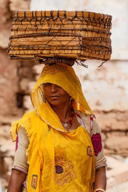 Osian, Hindistan - 22 Şubat 2015: Rajasthan'daki Osian'ın eski şehir merkezinde başında sepetle yürüyen kimliği belirsiz kadın