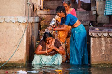 Varanasi, Hindistan - 18 Mart 2014. Varanasi 'nin eski ghatlarından kutsal Ganj Nehri' nde renkli geleneksel kıyafetleri ve Hindu dini yıkanma ritüelini gösteriyor.. 