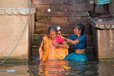 Varanasi, Hindistan - 18 Mart 2014. Varanasi 'nin eski ghatlarından kutsal Ganj Nehri' nde renkli geleneksel kıyafetleri ve Hindu dini yıkanma ritüelini gösteriyor.. 