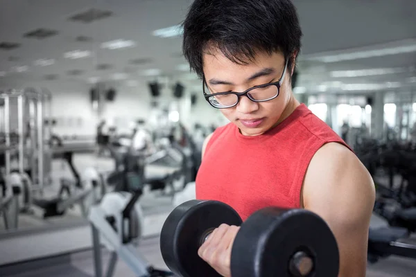 handsome young muscle man working with dumbbell in fitness room at gym for healthy and strong with blur background of fitness equipment in concept of sport, health, and lifestyle